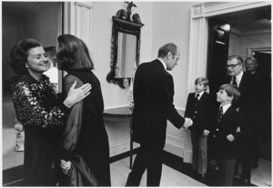 Photograph of First Lady Betty Ford and Happy Rockefeller Embracing as President Gerald Ford Greets Vice President Nelson A. Rockefeller and the Couple's Two Sons